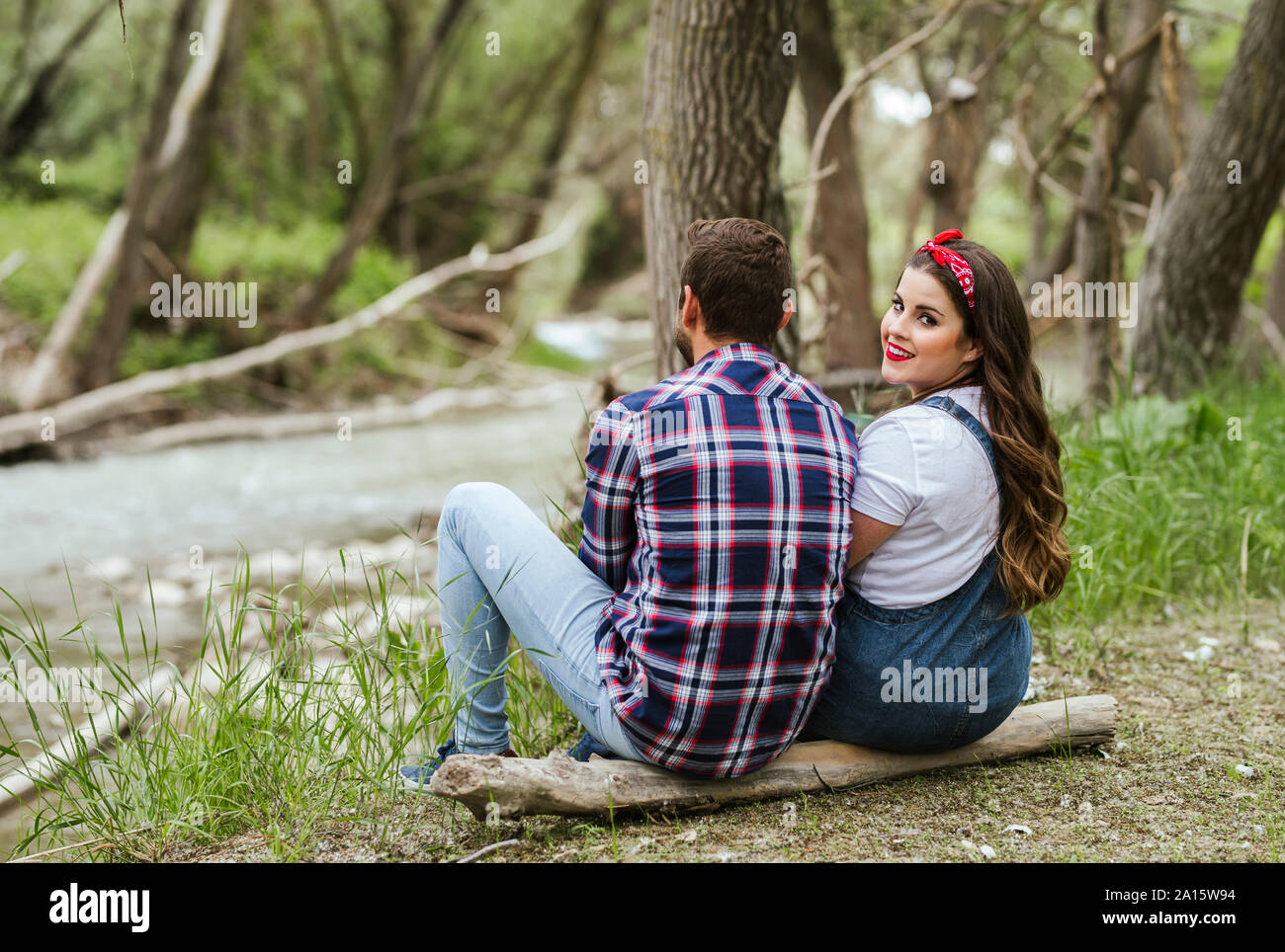 Junges Paar nebeneinander sitzen auf einem Baumstamm Stockfoto