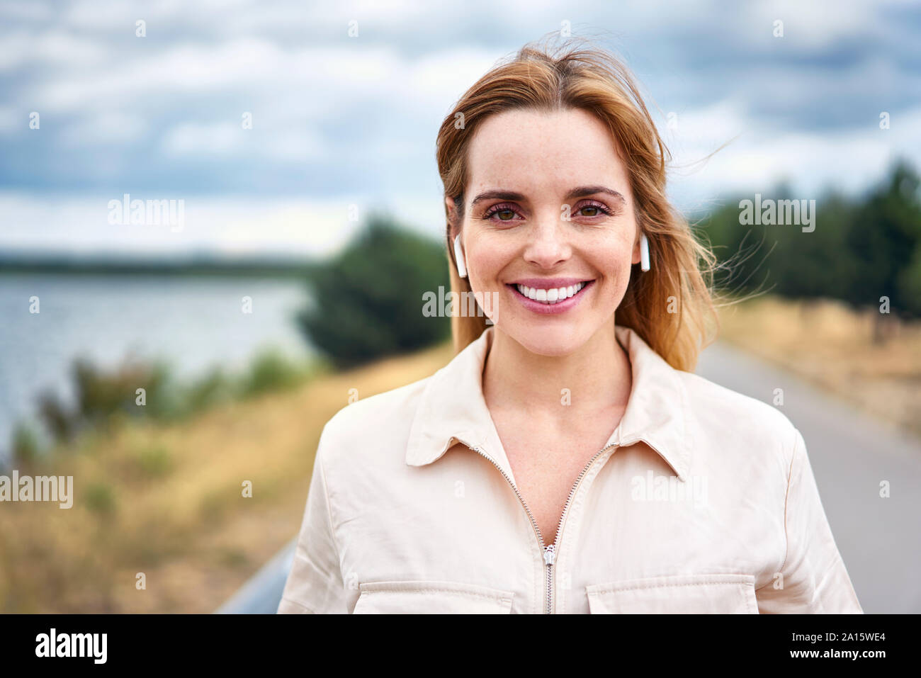 Porträt der lächelnde Frau mit drahtlosen Kopfhörern in der Natur Stockfoto