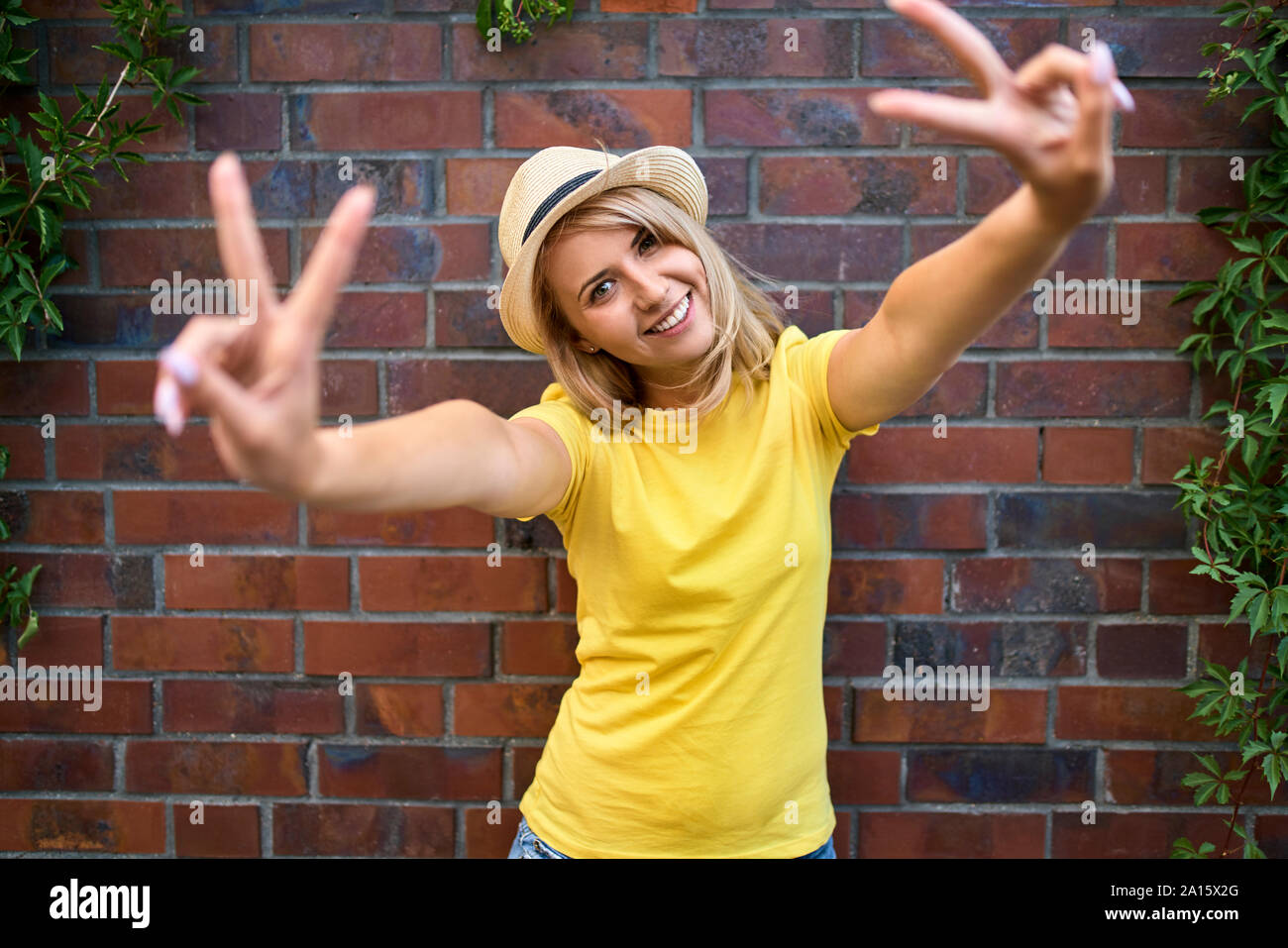 Porträt der glückliche junge Frau, die an einer Mauer Making Peace Zeichen Stockfoto