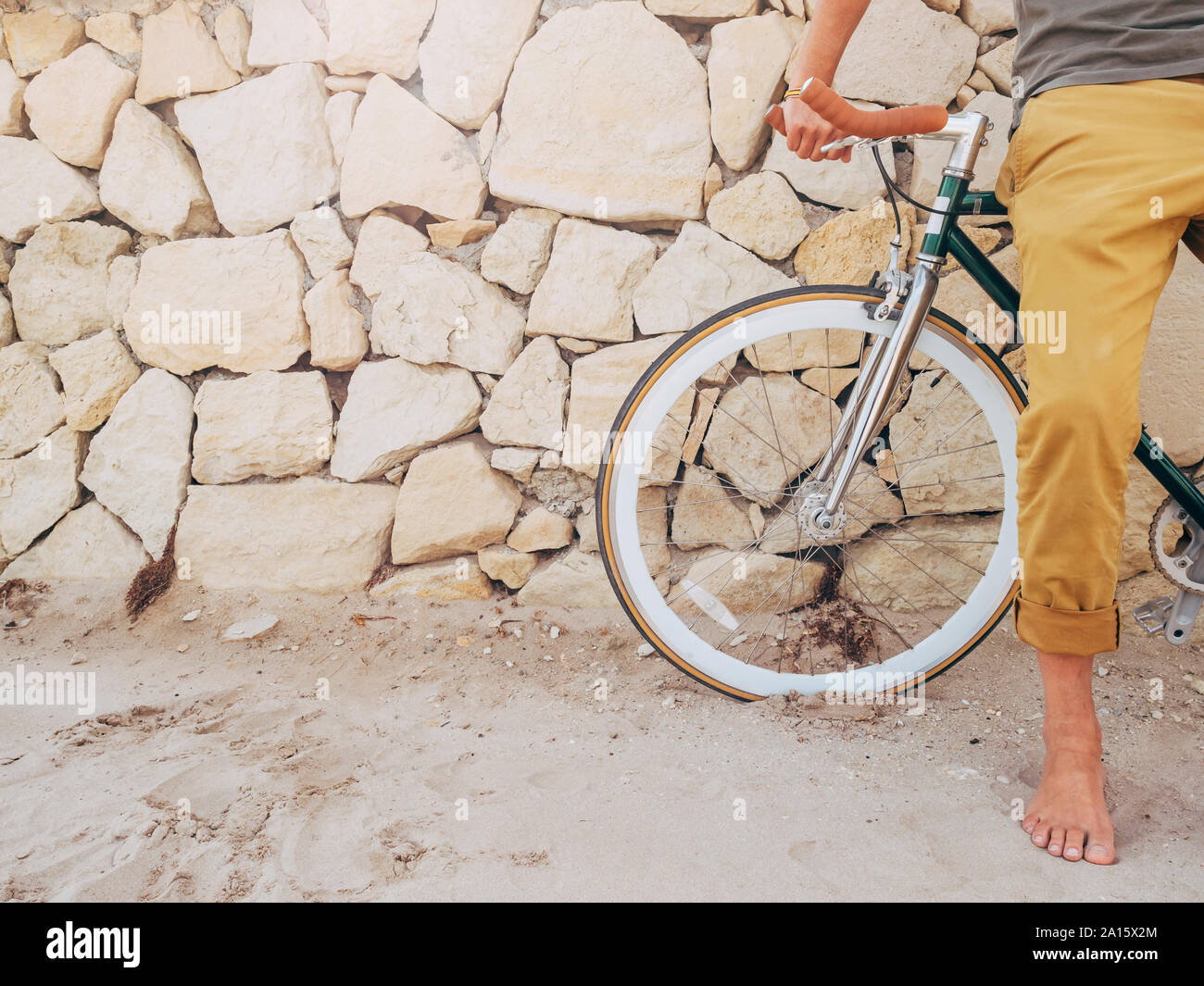 Barfuß Mann mit Fixie bike vor natursteinmauer am Strand, teilweise mit Blick Stockfoto