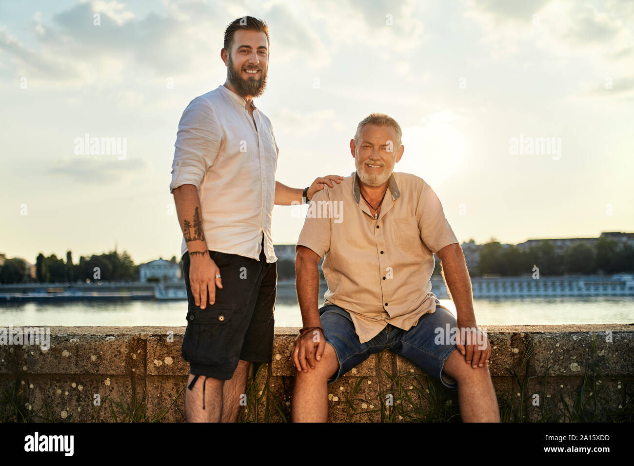 Portrait von lächelnden Vater und erwachsener Sohn am Flußufer bei Sonnenuntergang Stockfoto