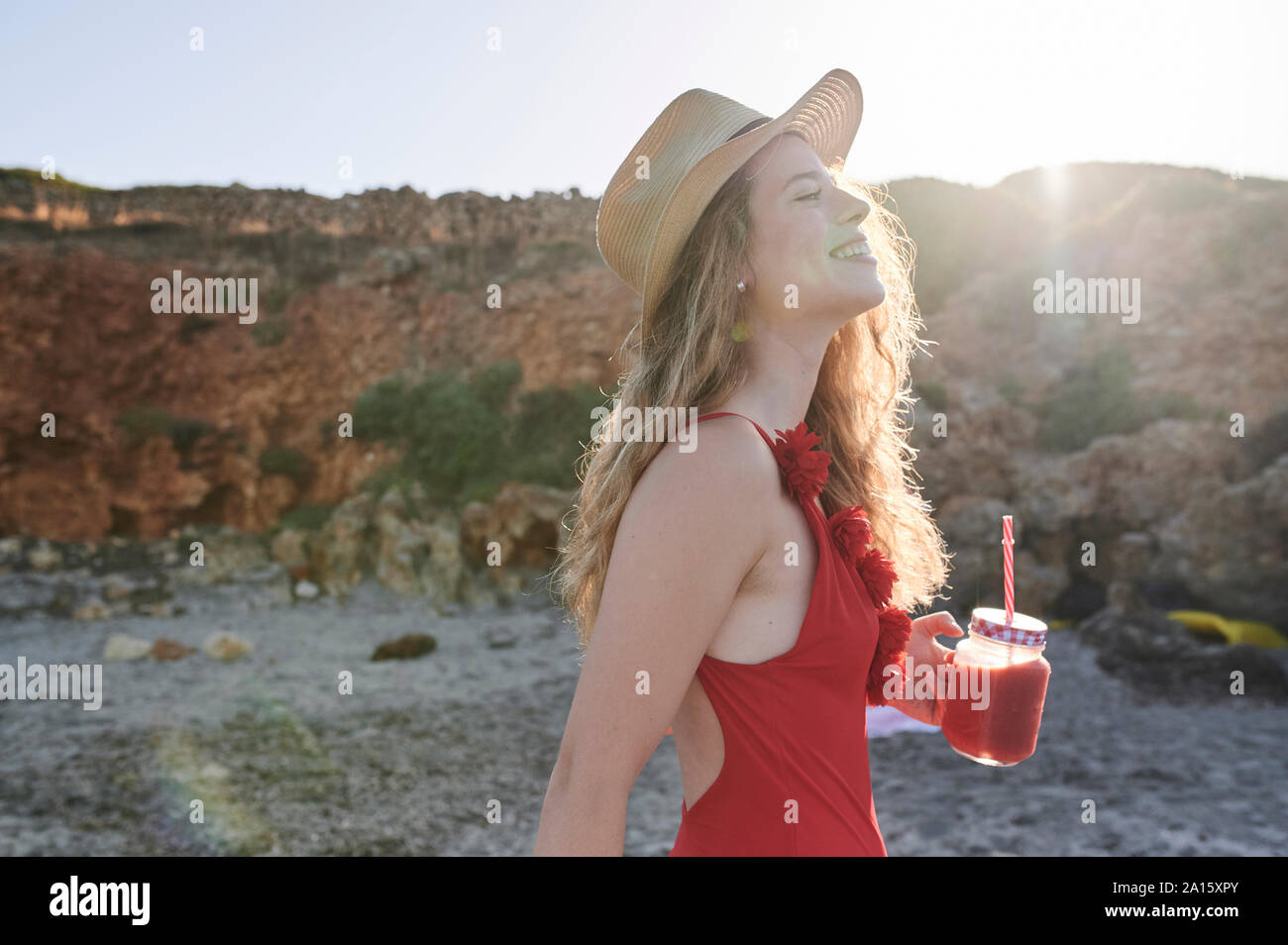 Glückliche junge Frau mit einem Smoothie zu Fuß am Strand Stockfoto