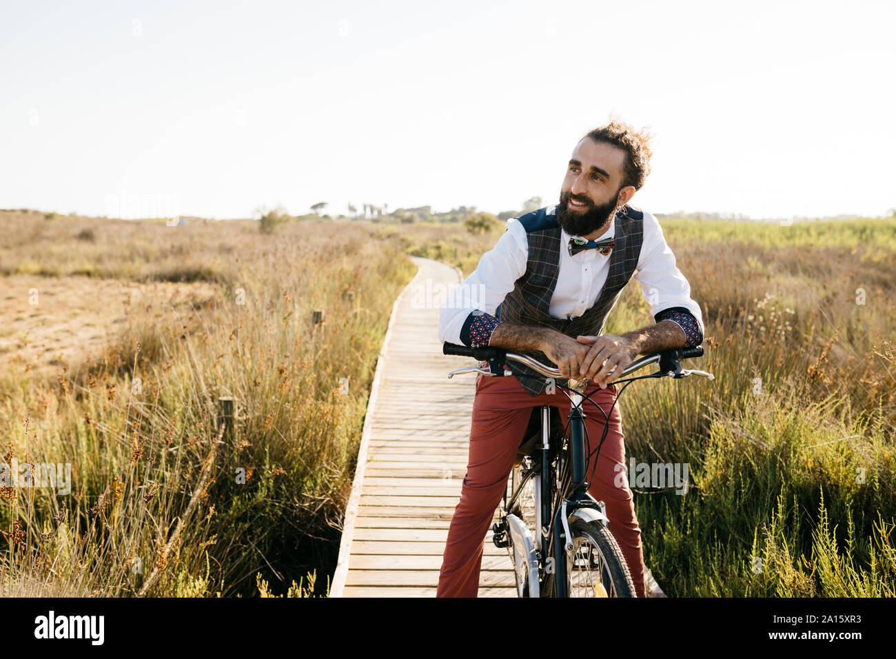 Gut gekleideter Mann mit seinem Fahrrad auf einem Holzsteg in der Landschaft mit einer Unterbrechung Stockfoto