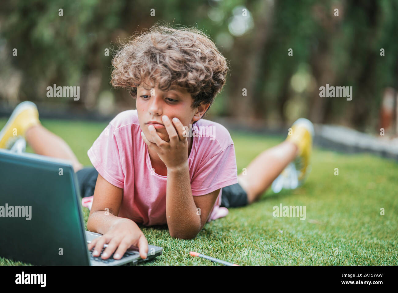 Junge im Gras liegend mit Laptop Stockfoto