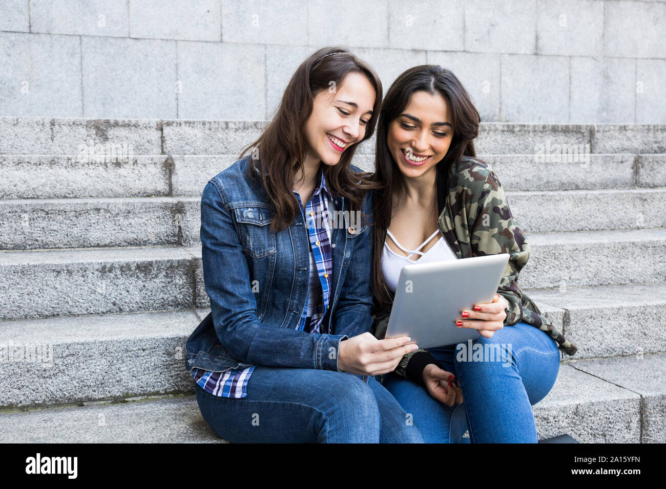 Glückliche junge Frauen beobachten Tablette auf Schritte gemeinsam in Madrid, Spanien Stockfoto
