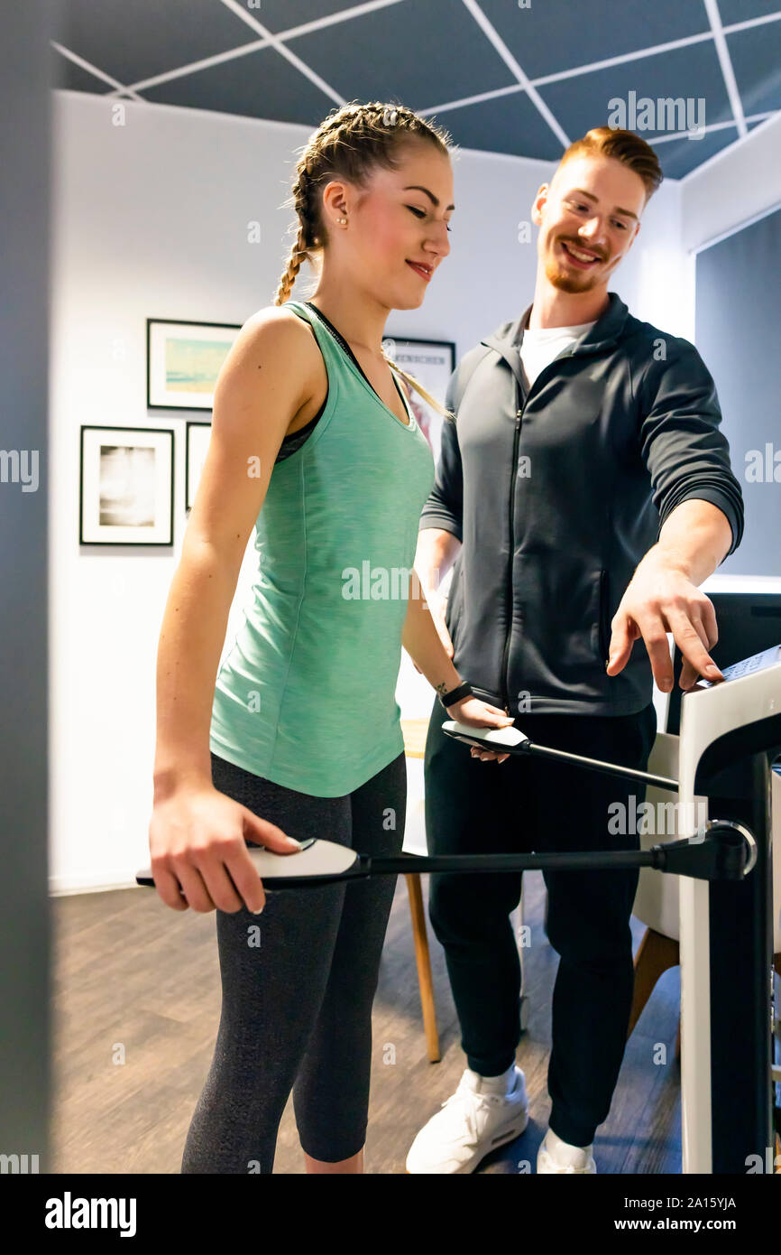 Junge Frau mit persönlichem Trainer im Fitnessraum auf Körper Analyse Gerät Stockfoto