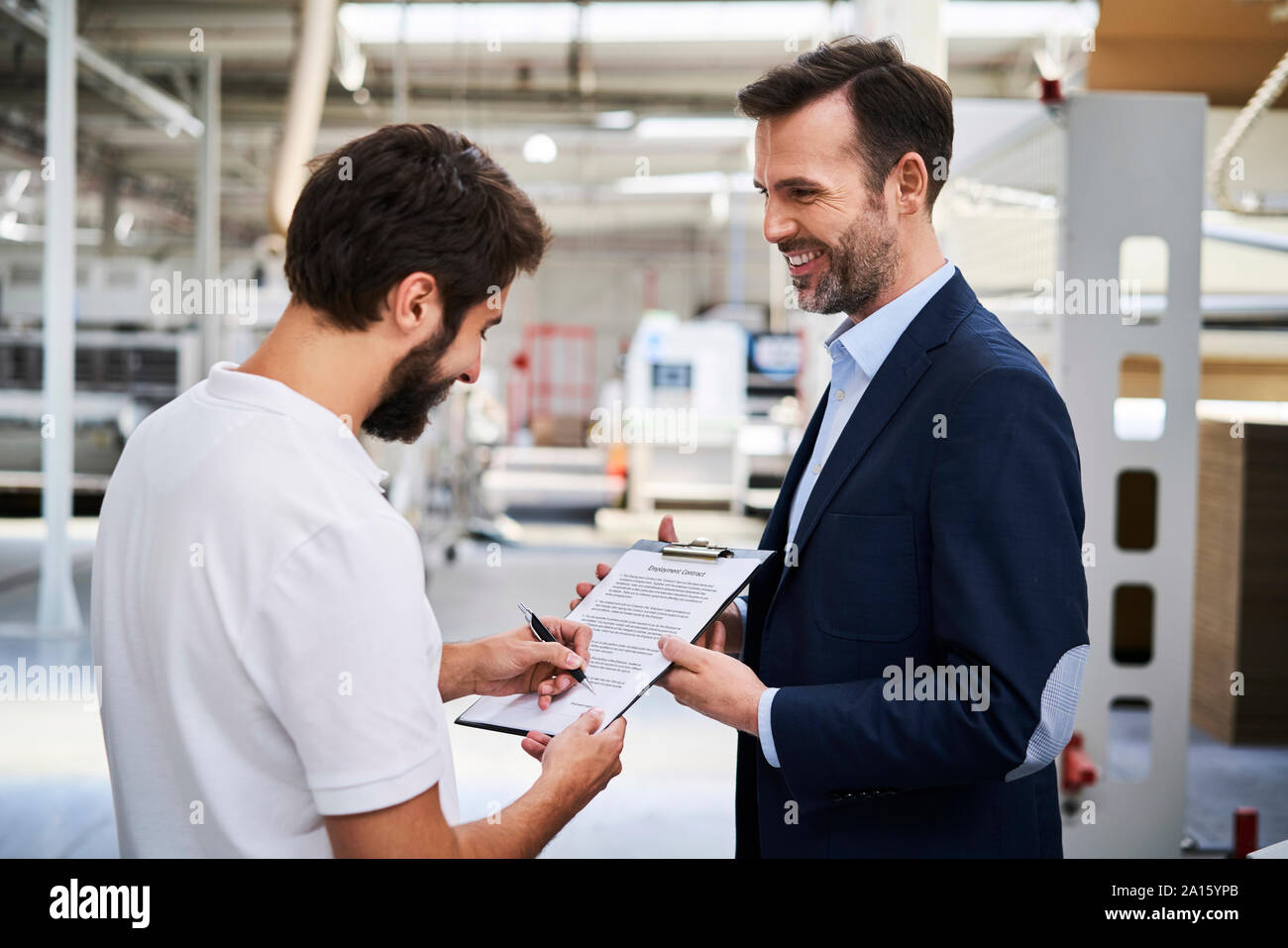 Mitarbeiter Unterzeichnung Dokument in Fabrik durch Geschäftsmann gehalten Stockfoto