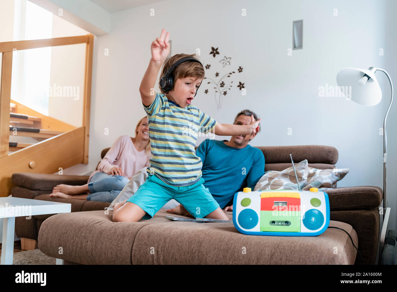 Begeistert junge Musik hören mit Kopfhörern auf der Couch zu Hause mit Eltern im Hintergrund Stockfoto