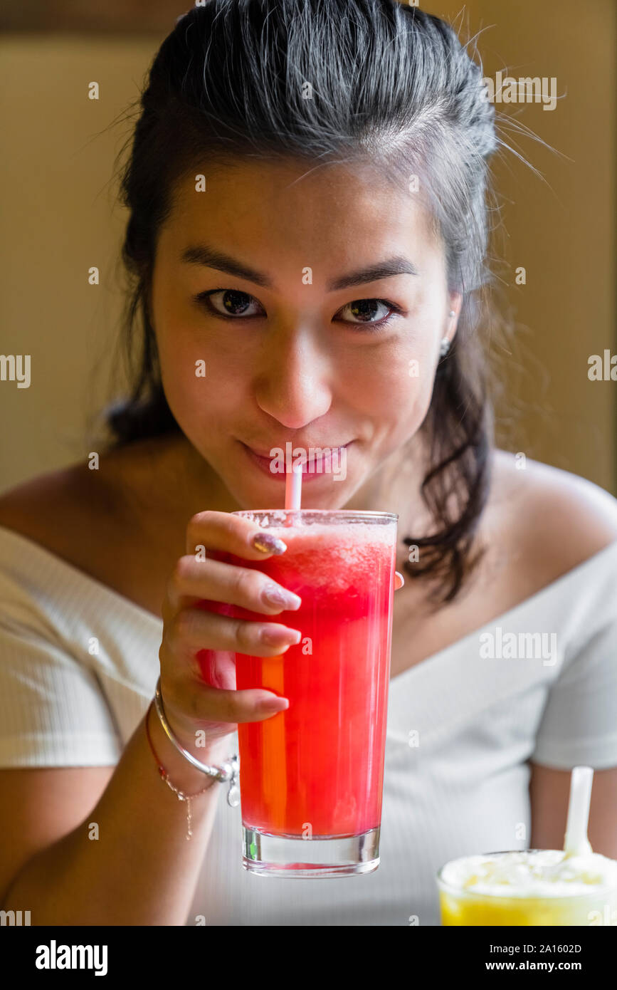 Porträt der lächelnde junge Frau trinkt einen Smoothie Stockfoto