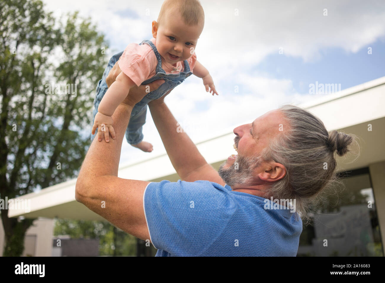 Gerne reifer Mann anheben Baby Mädchen im Garten seines Hauses Stockfoto