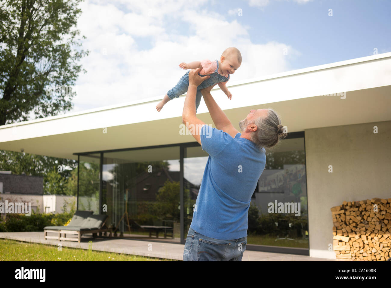 Gerne reifer Mann anheben Baby Mädchen im Garten seines Hauses Stockfoto