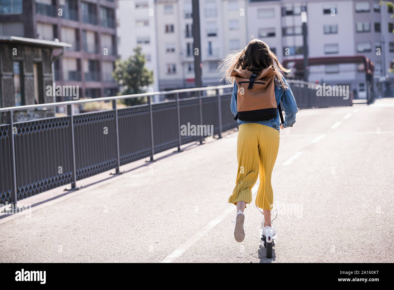 Ansicht der Rückseite des jungen Frau reiten Elektroroller auf einer Brücke Stockfoto