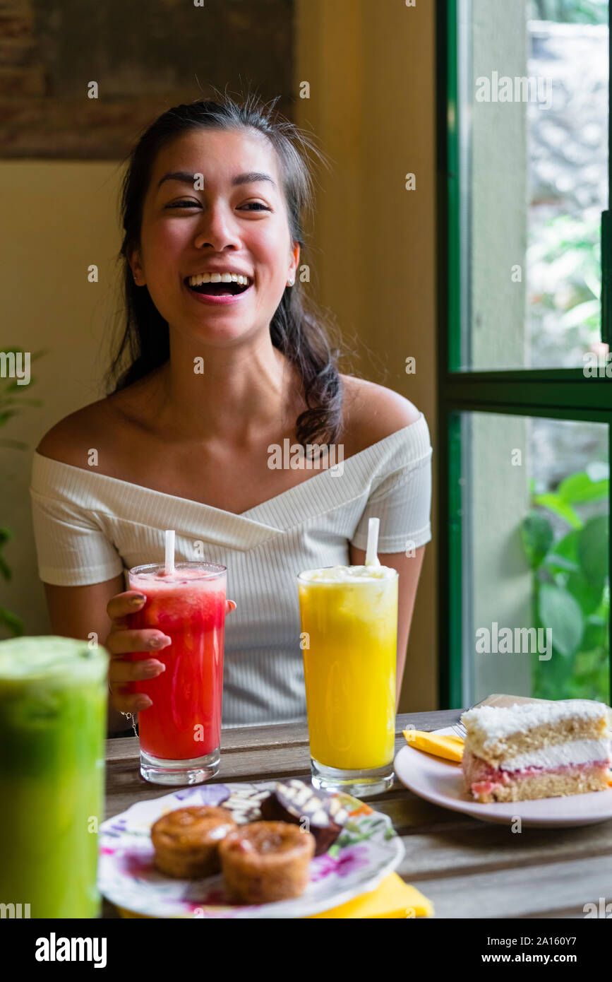 Lachende junge Frau trinkt einen Smoothie in einem Cafe Stockfoto