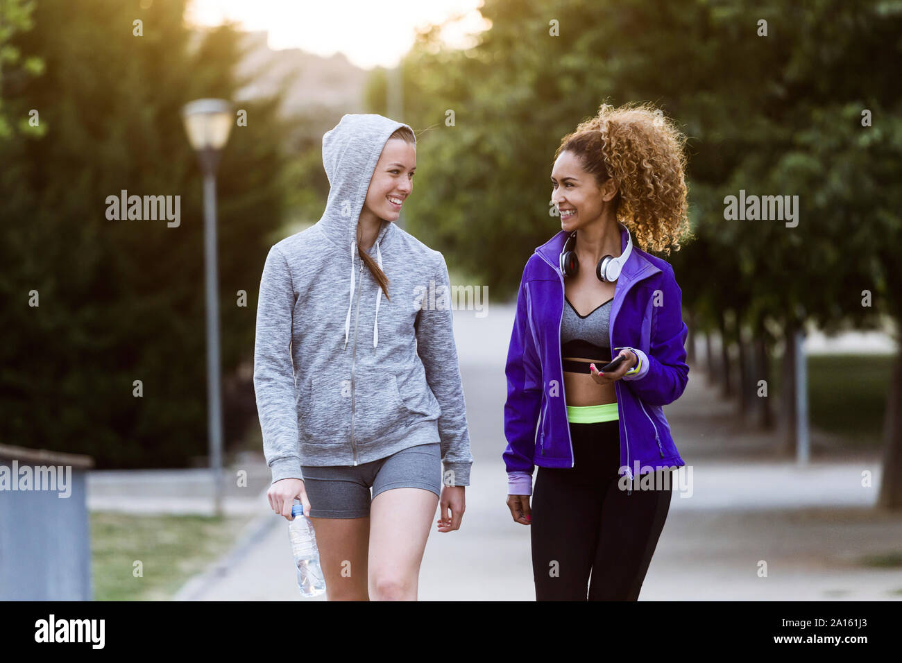 Zwei lächelnde sportliche junge Frauen wandern im Park nach dem Workout Stockfoto