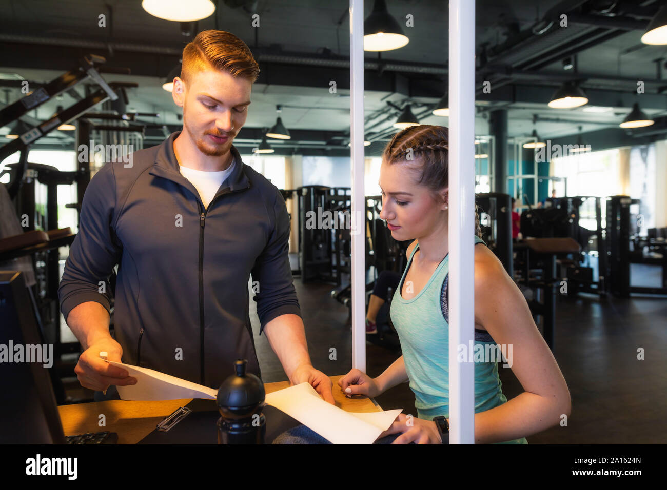 Junge Frau und Personal Trainer diskutieren Plan im Fitness Gym Stockfoto