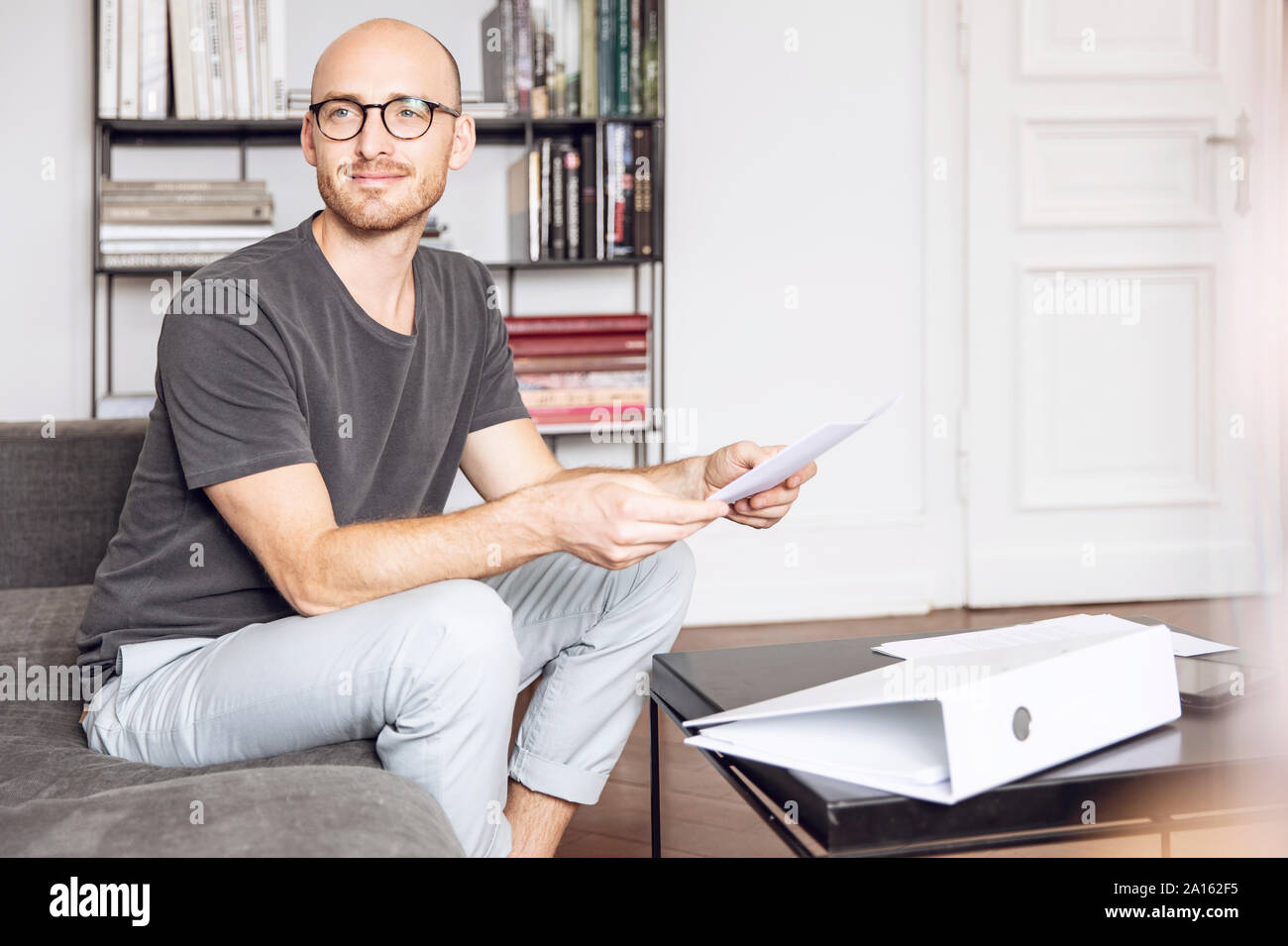 Mann sitzt zu Hause auf der Couch mit einem Blatt Papier Stockfoto