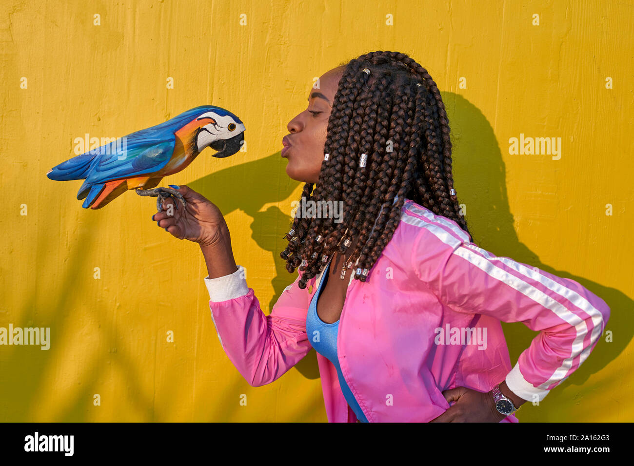 Frau Küssen eines hölzernen Papagei auf einem gelben wand Stockfoto