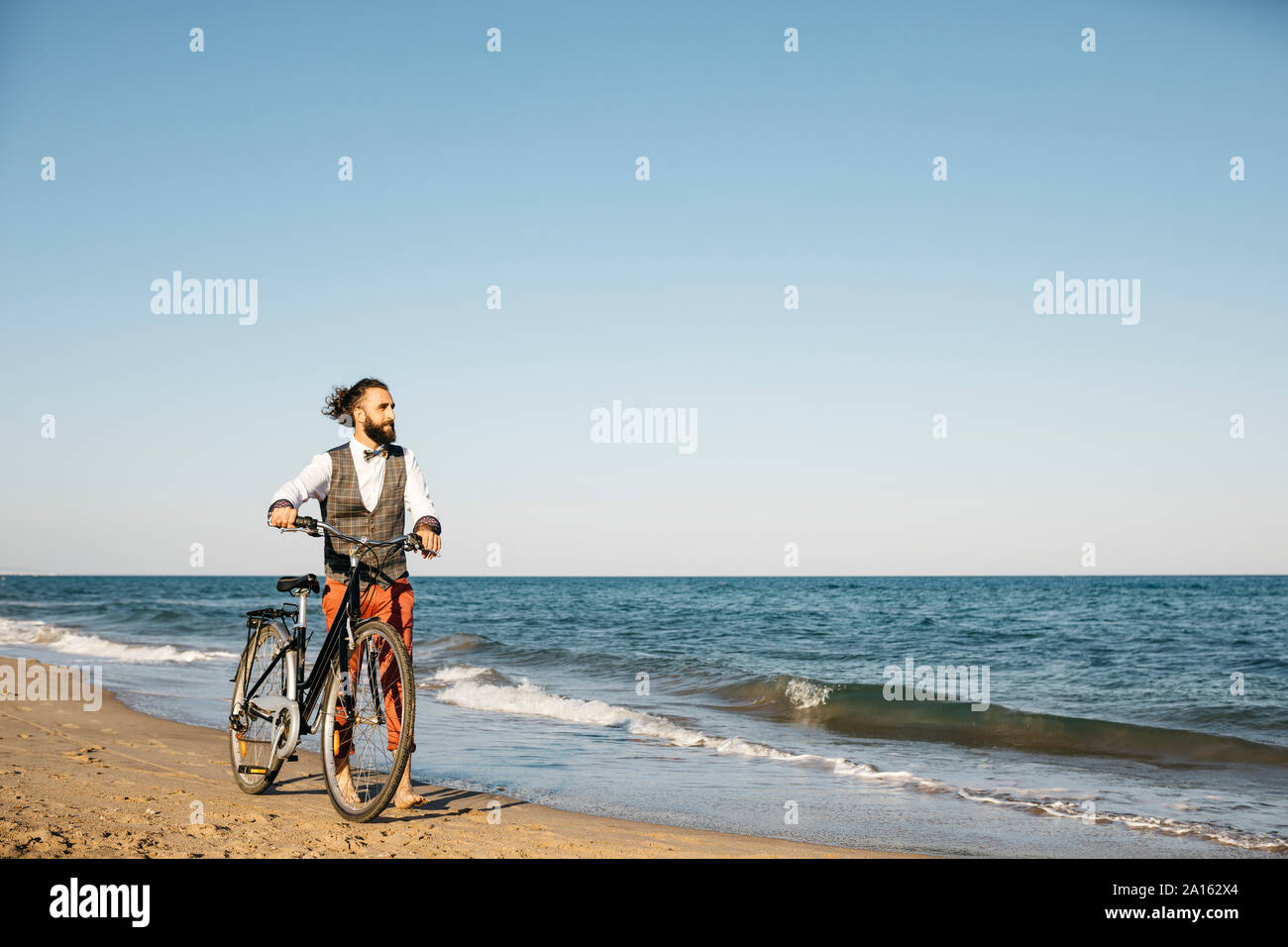Gut gekleideter Mann mit seinem Fahrrad am Strand Stockfoto