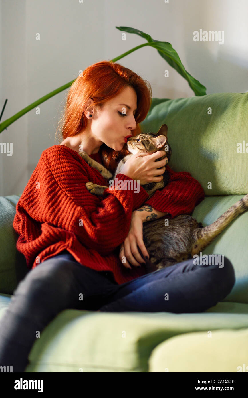 Rothaarige Frau mit Katze auf der Couch zu Hause Stockfoto