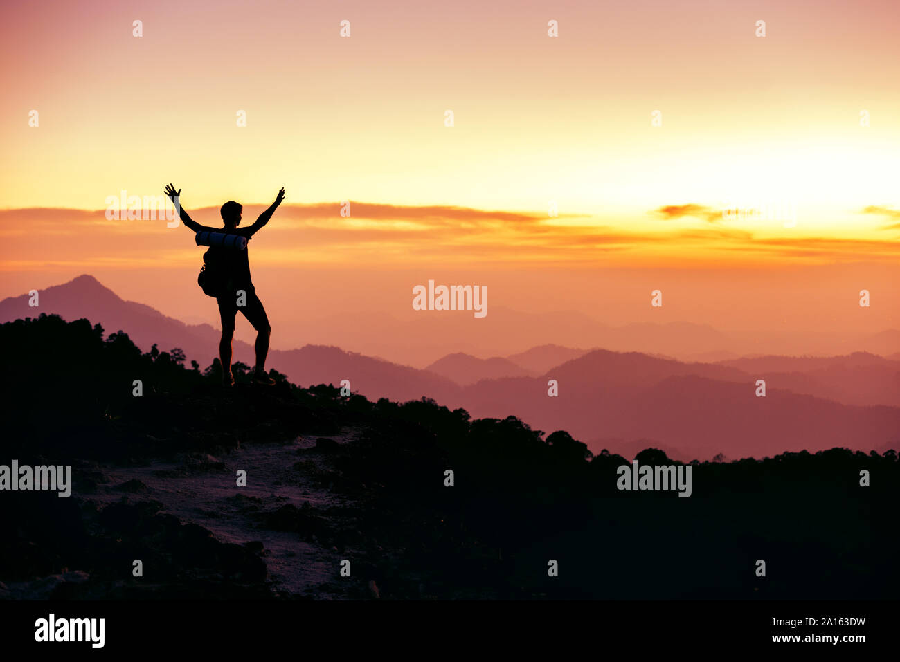 Wanderer oder Reisende Silhouette steht auf Berggipfel gegen Sonnenuntergang Mit angehobenen Armen Stockfoto