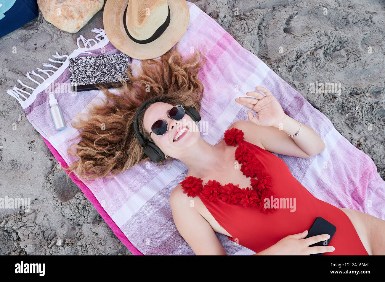 Glückliche junge Frau liegen auf dem Handtuch am Strand Hören von Musik Stockfoto