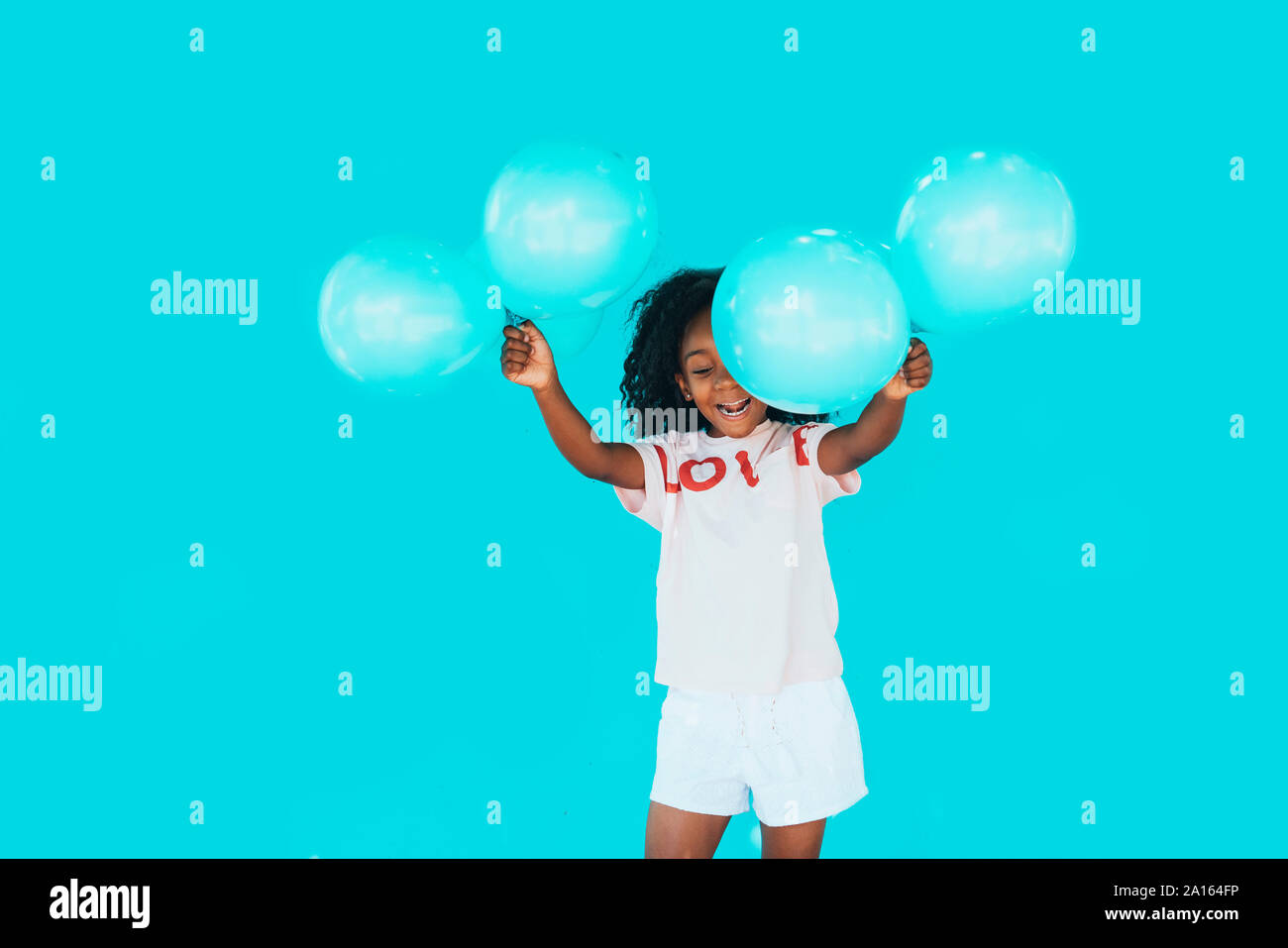 Kleine Mädchen vor einer blauen Wand, holding Ballons Stockfoto