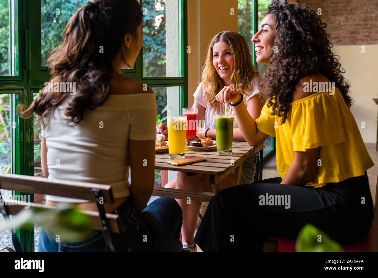 Drei glückliche junge Frauen mit Smoothies treffen in einem Cafe Stockfoto