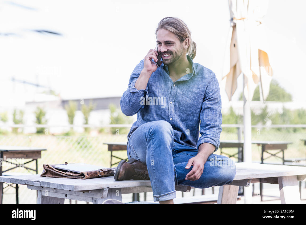 Junge Mann sitzt am Tisch in einem Biergarten, am Telefon zu sprechen Stockfoto