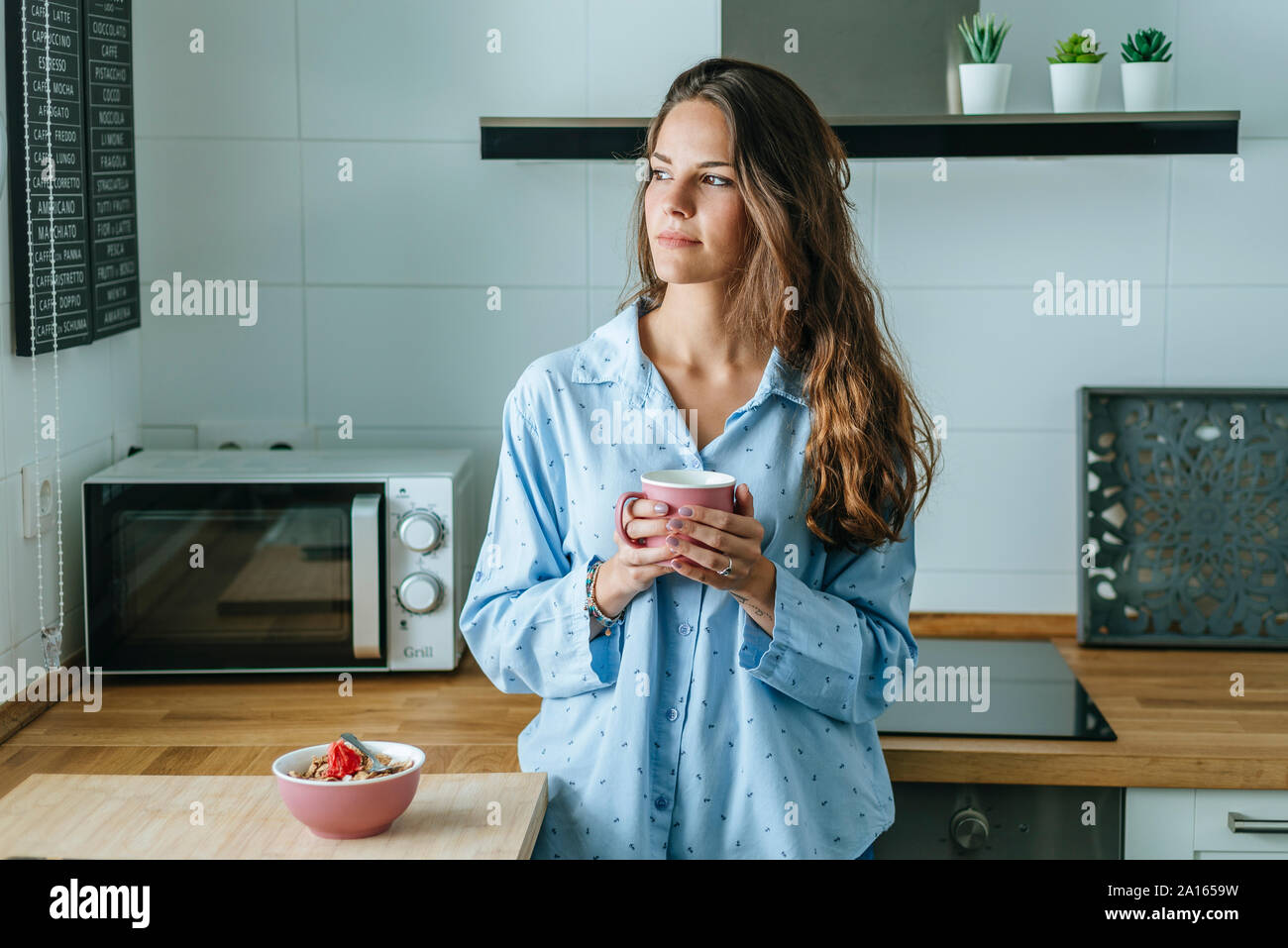 Porträt der jungen Frau mit Pyjama in der Küche zu Hause holding Tasse Kaffee Stockfoto