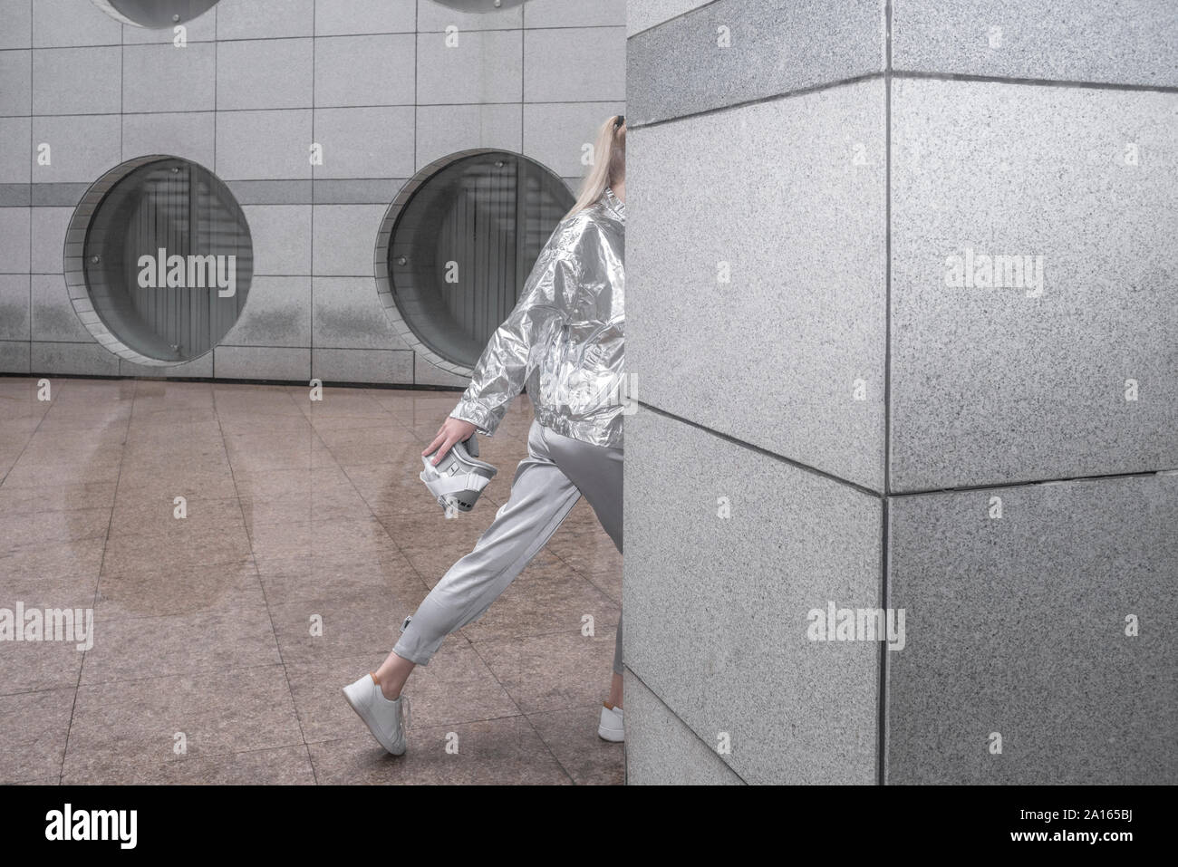 Mädchen in Silber passt zu Fuß hinter der Wand in der futuristischen Stadt Stockfoto
