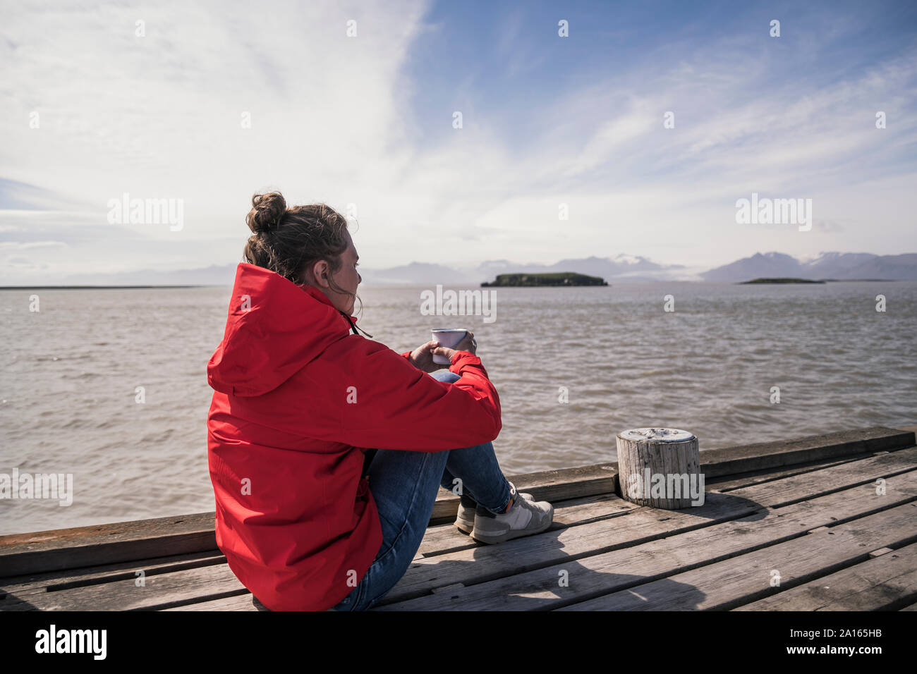 Junge Frau sitzt auf einem Steg, trinken Kaffee, South East Iceland Stockfoto