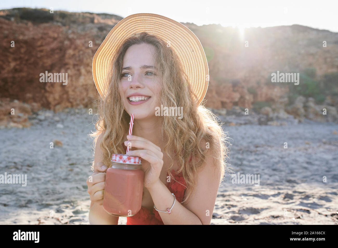 Glückliche junge Frau mit einem Smoothie am Strand Stockfoto