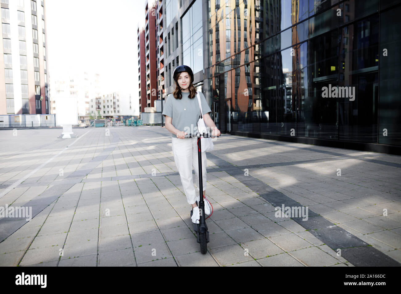 Frau mit e-Scooter und Helm, moderne Bürogebäude im Hintergrund Stockfoto