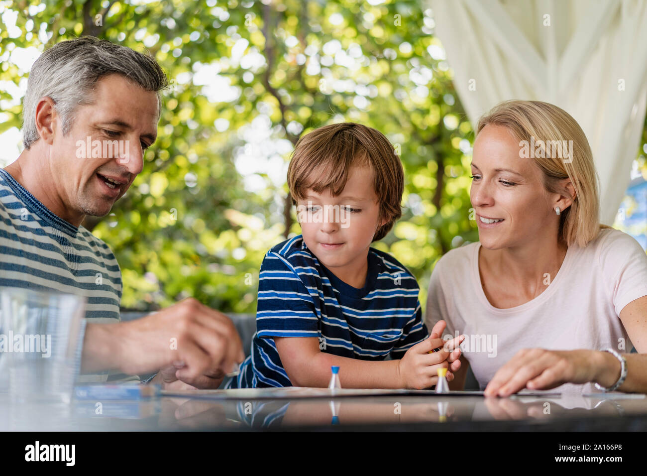 Glückliche Eltern und Sohn spielen ein Brettspiel auf der Terrasse Stockfoto