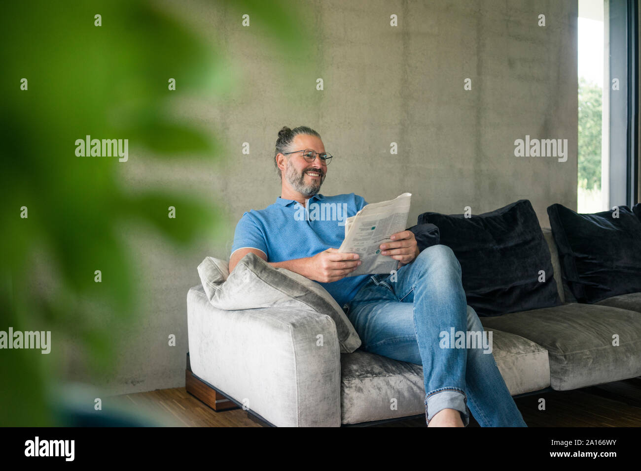 Lächelnd reifer Mann saß auf der Couch zu Hause lesen Zeitung Stockfoto