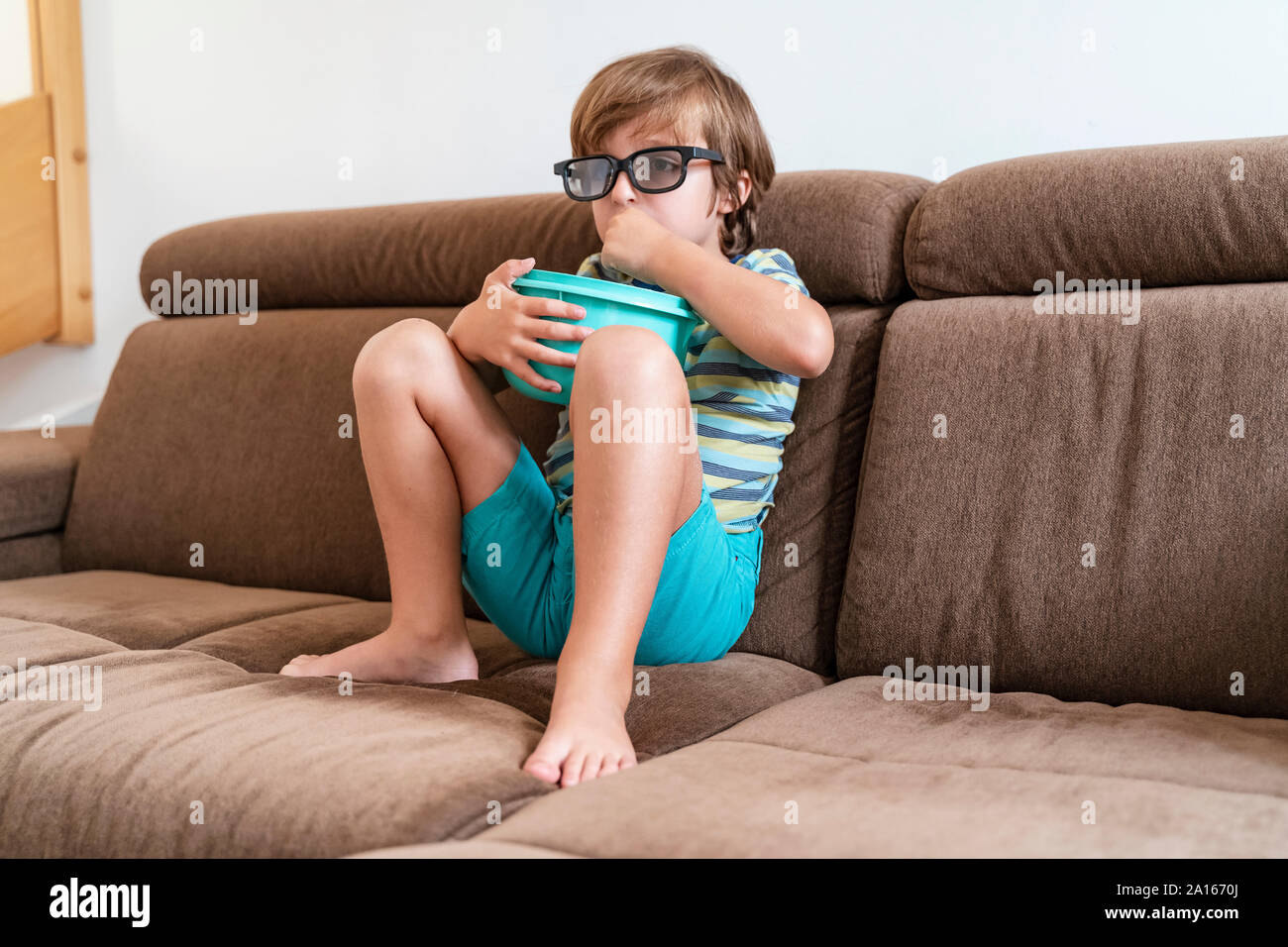 Junge sitzt auf der Couch zu Hause tragen 3D-Brille und essen Popcorn Stockfoto