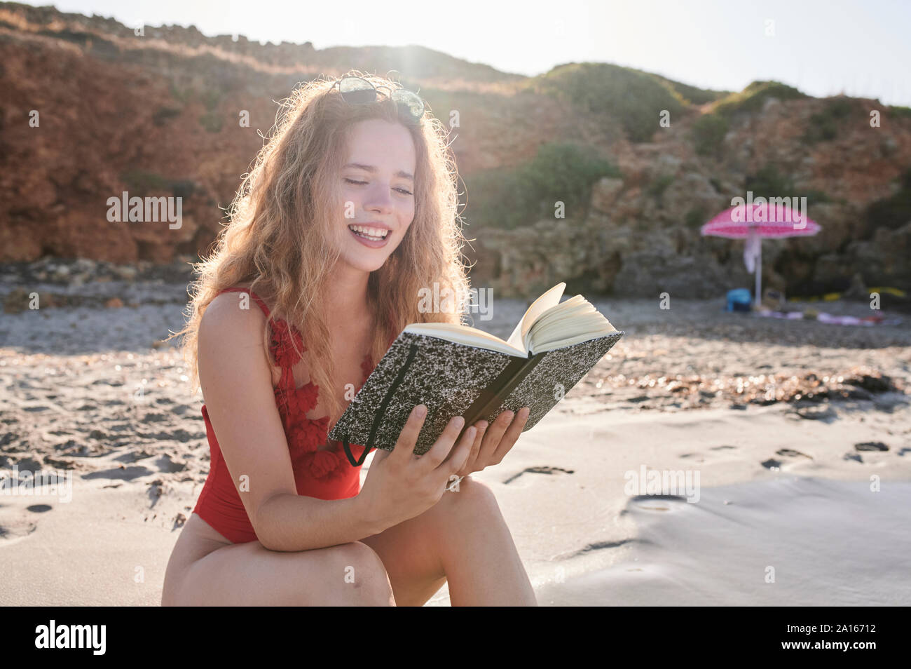 Glückliche junge Frau liest Buch am Strand Stockfoto