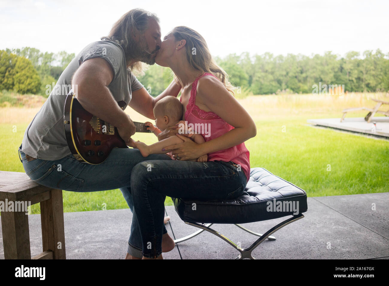 Mann mit Gitarre küssen Frau mit Baby Mädchen sitzen auf dem Schoß Stockfoto