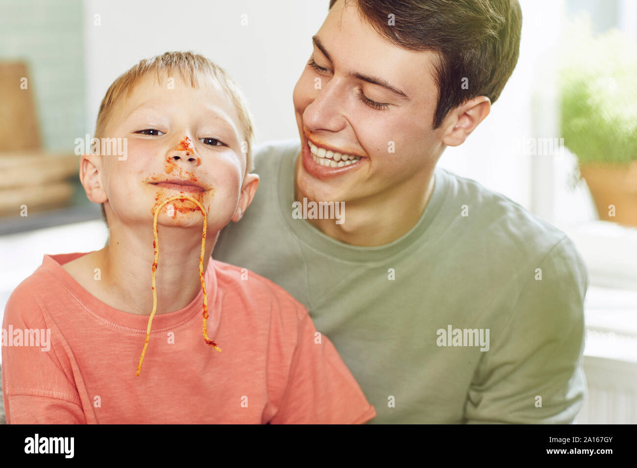 Kleiner Bruder mit Gesicht voller Tomatensauce, auf den Schoß von seinem großen Bruder Stockfoto