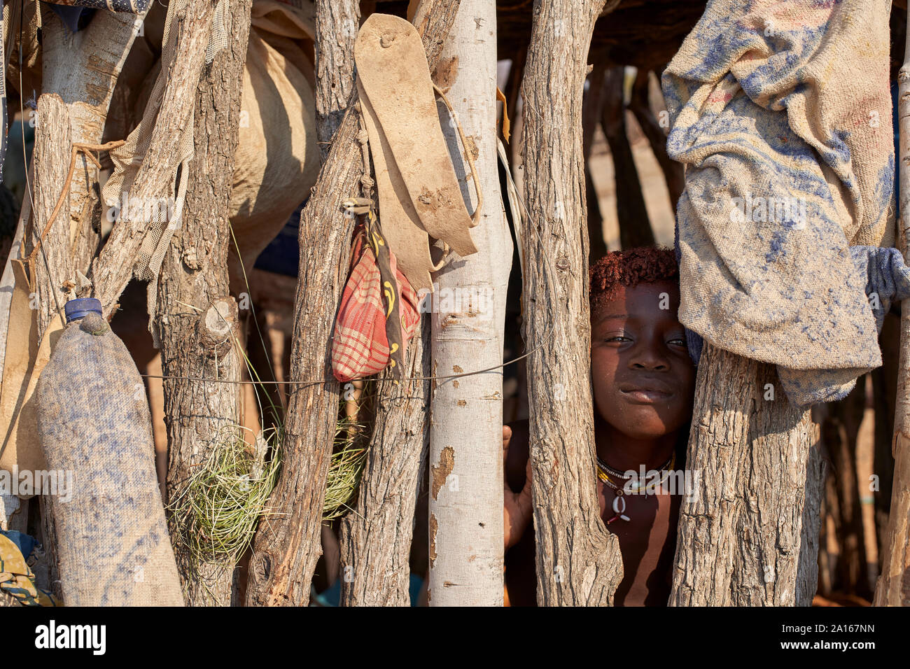 Mucubal Mädchen versteckt sich hinter Holzzaun, Tchitundo Hulo, Virei, Angola Stockfoto