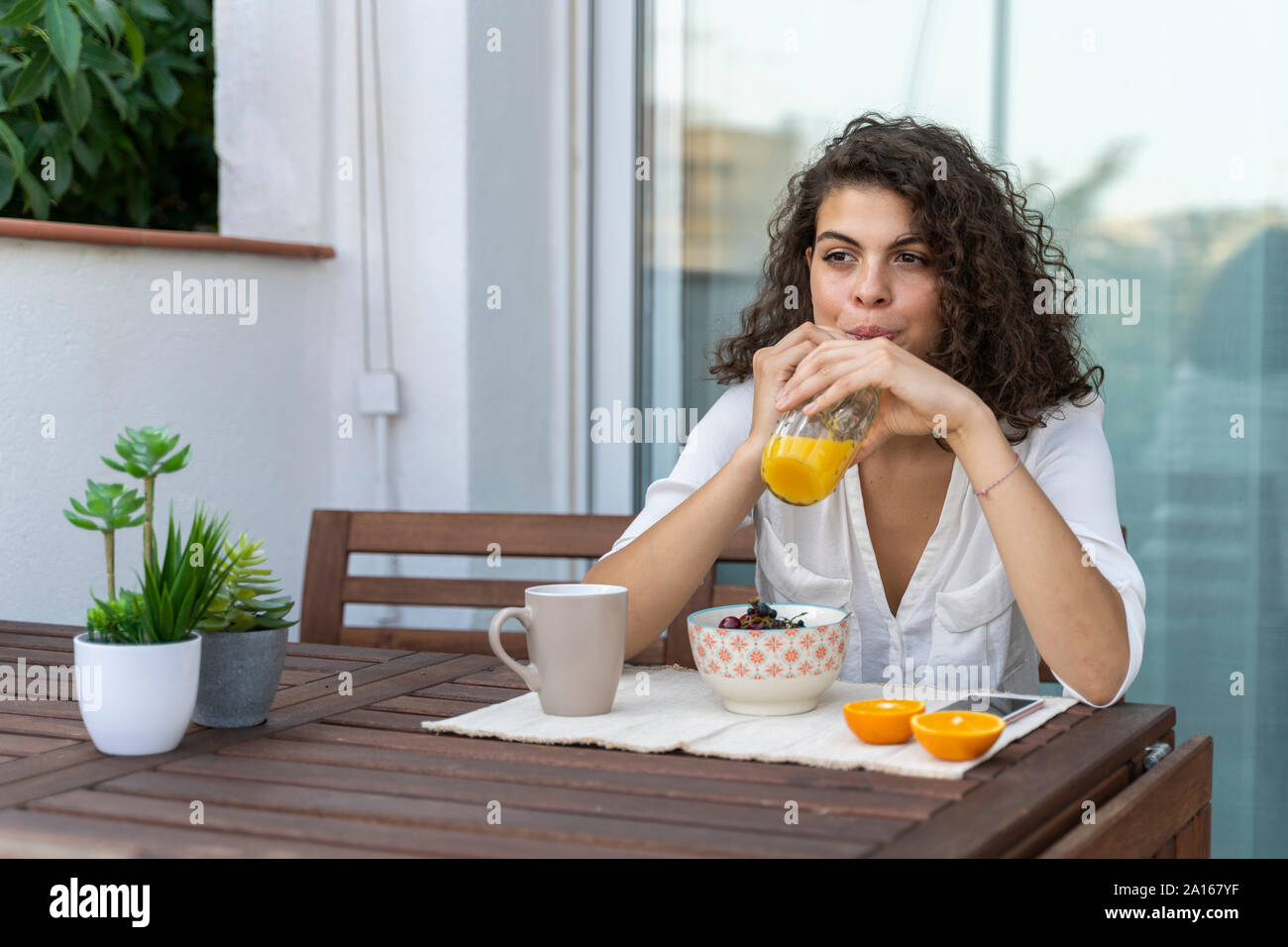 Junge Frau trinkt Orangensaft auf dem Balkon Stockfoto