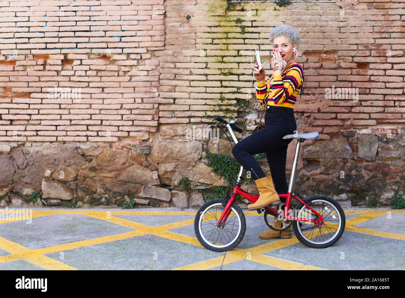 Modische reife Frau mit Fahrrad und Smartphone auf der Straße Stockfoto