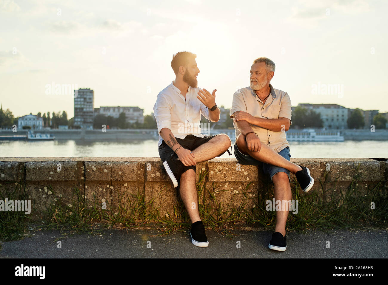 Vater und Sohn sitzen auf einer Mauer an der Riverside sprechen Stockfoto