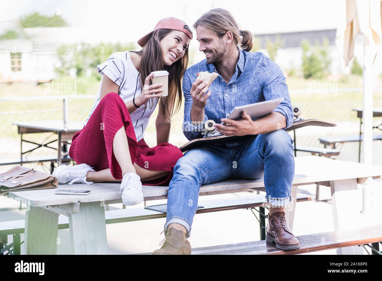 Junges Paar sitzen am Tisch in einem Biergarten mit Tablet, Sandwich und Kaffee zum Mitnehmen Stockfoto