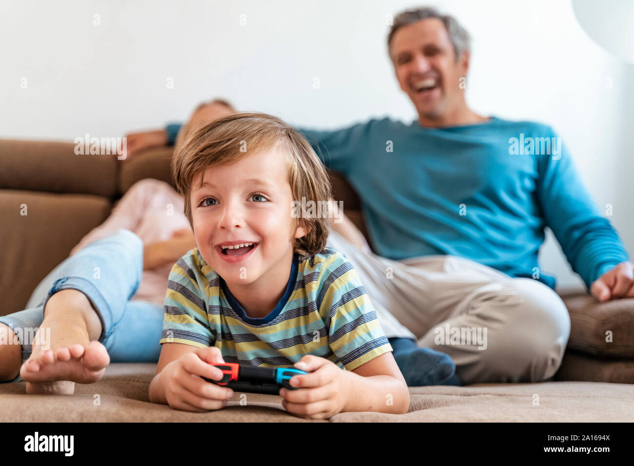 Junge liegen auf der Couch zu Hause spielen video game mit Eltern beobachten Stockfoto