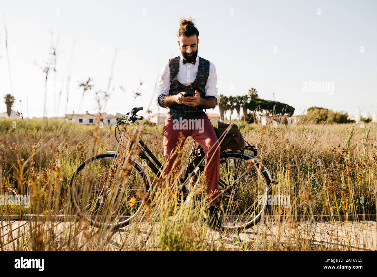 Gut gekleideter Mann mit seinem Fahrrad auf einem Holzsteg in der Landschaft mit Handy Stockfoto
