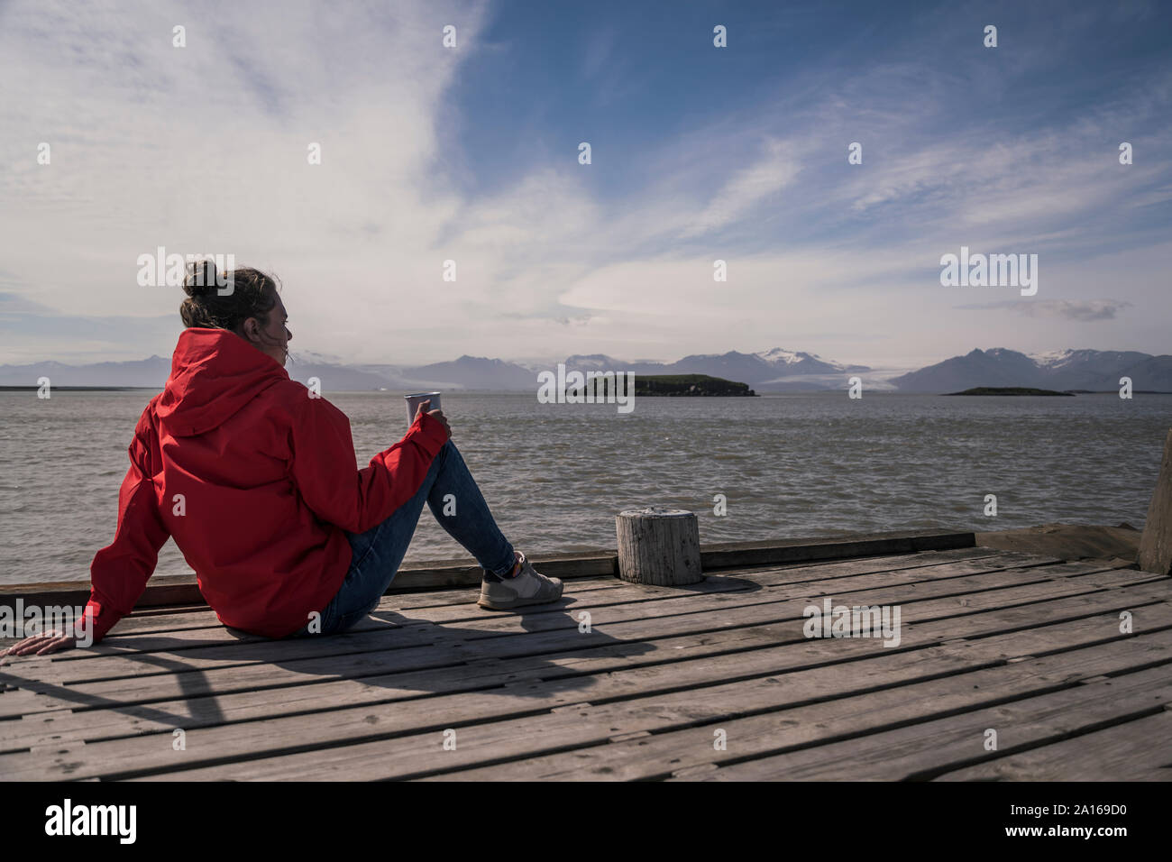 Junge Frau sitzt auf einem Steg, mit Blick auf das Meer, South East Iceland Stockfoto