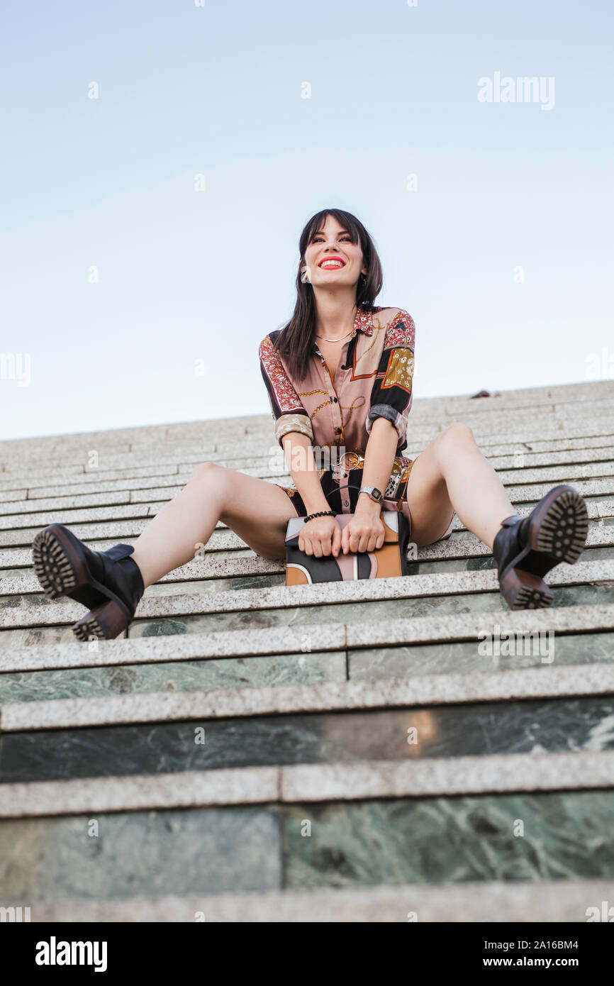 Junge Frau mit gemusterten Kleid sitzt auf der Treppe Stockfoto