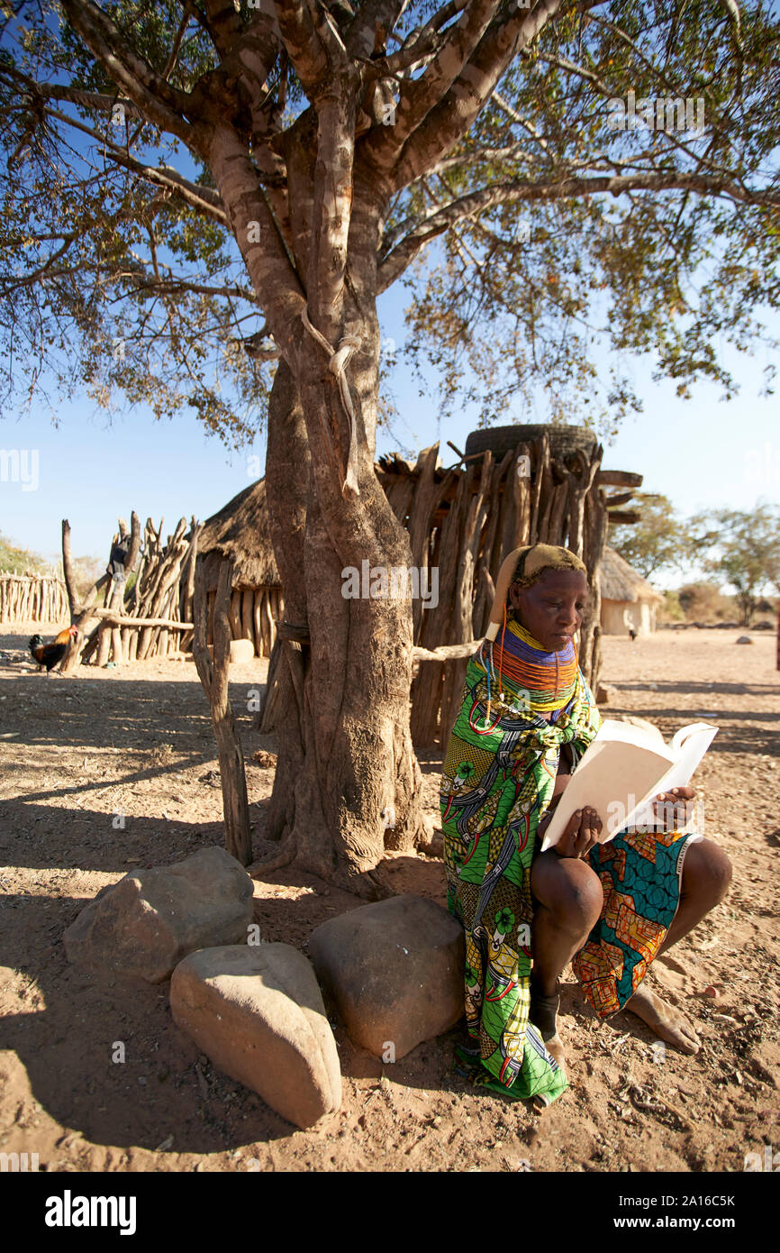 Traditionelle muhila Frau, sitzen unter Baum, ein Buch lesen, Kehamba, Chibia, Angola Stockfoto
