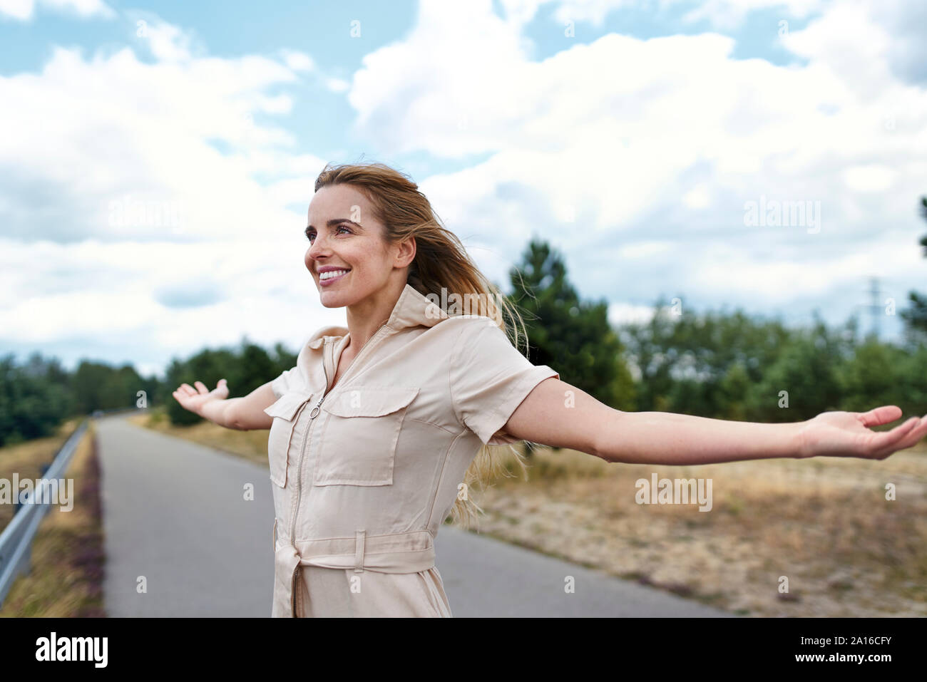 Glückliche Frau steht auf einer Landstraße mit ausgestreckten Armen Stockfoto